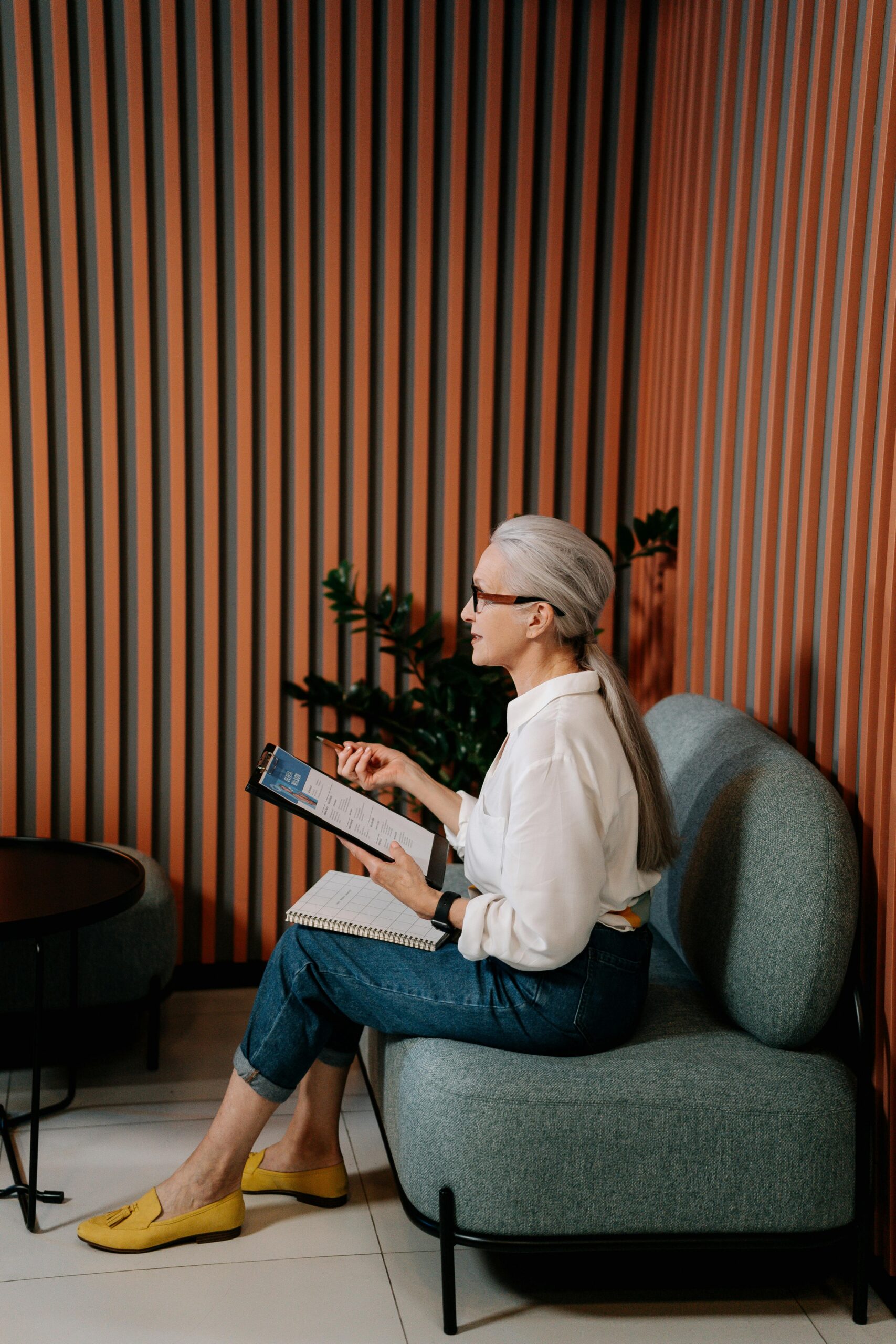 An adult woman in casual attire reviewing notes on a tablet in a stylish office setting.